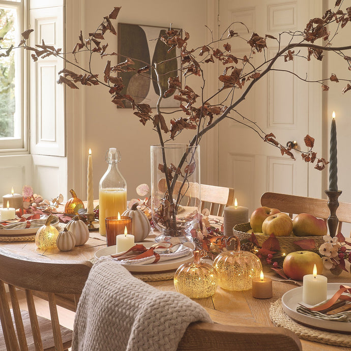 Herbstlich gedeckter Tisch mit leuchtenden Kürbissen, Kerzen und Zweigen als stimmungsvolle Deko.