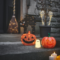 Halloween-Deko mit leuchtenden Kürbissen, Geist, Katze, Hexenbesen und Kerzen vor einer Haustür.