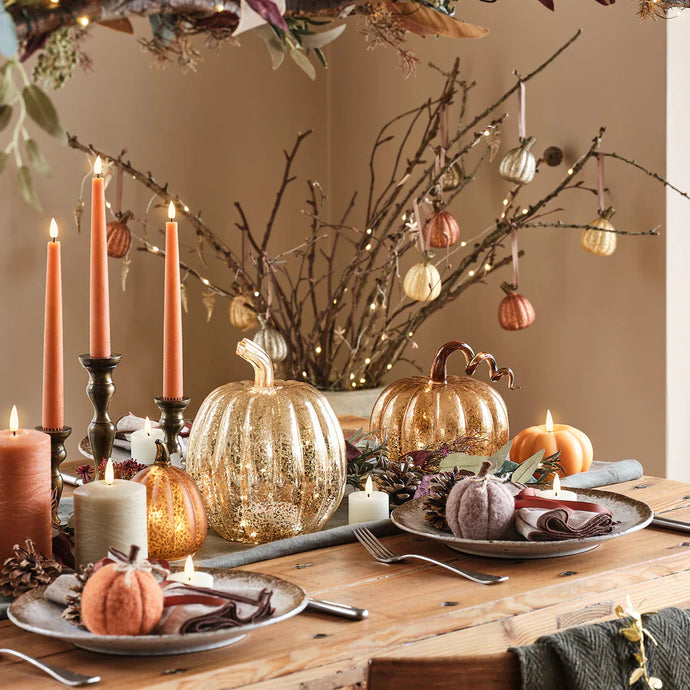 Herbstlich gedeckter Tisch mit leuchtenden Kürbissen, Kerzen und Zweigen als stimmungsvolle Deko.