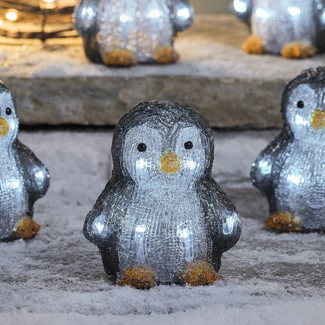 Niedliche glitzernde Pinguin-Dekofigur mit grauem Schneeeffekt-Finish, goldenen Akzenten und weißen Augen, positioniert auf Stein-Untergrund mit unscharfem Hintergrund – festliche Weihnachtsfigur für Außendekoration, Garten-Arrangements und winterliche Hausdekorationen mit charmanter Schneekristall-Textur.