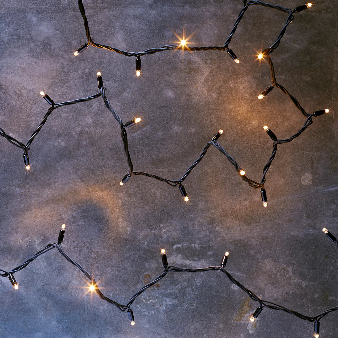 Warmweiße LED-Lichterkette mit schwarzem Kabel auf grauem Steinboden